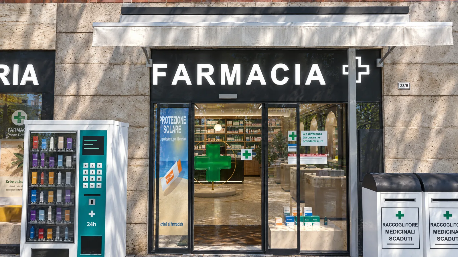 Ricostruzione 3D dell’ingresso vero: le porte scorrevoli sotto la tenda e l’insegna FARMACIA, tra il distributore e i raccoglitori dei farmaci scaduti, si aprono sull’interno.